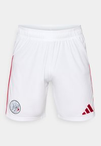 Shorts de sport blancs en tissu lisse, avec des rayures latérales rouges et un logo circulaire sur la cuisse gauche arborant un emblème sportif.