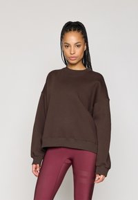Sweatshirt oversized castanho com decote redondo e ombros caídos, combinado com leggings bordô com riscas texturizadas.