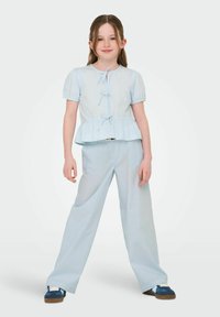 Haut peplum bleu clair avec des manches courtes bouffantes et un détail de cravate à l'avant, associé à un pantalon large bleu clair et des baskets bleues.