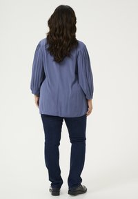 Maglione azzurro chiaro con maniche a sbuffo, tessuto strutturato e taglio dritto, abbinato a jeans blu scuro e scarpe nere.