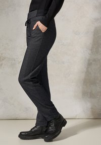 Pantalons gris foncé texturés avec une taille élastique à cordon, poches latérales et coupe slim, associés à des bottes noires à lacets.