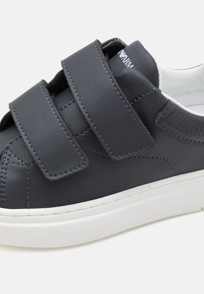 Mörkblå lädersneakers med två breda kardborreband, vit sula och subtila sömdetaljer, med en slät yta och rundad form.