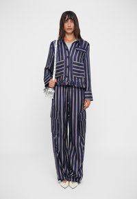 Set a righe blu navy e rosa composto da una camicia con colletto e bottoni, pantaloni con vita elastica e tasche laterali, e scarpe bianche con punta.