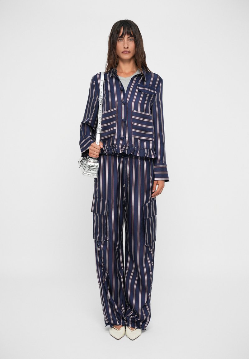 Set a righe blu navy e rosa composto da una camicia con colletto e bottoni, pantaloni con vita elastica e tasche laterali, e scarpe bianche con punta.