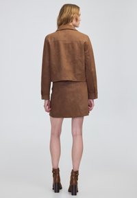 Chaqueta recortada de color marrón con textura combinada con una falda a juego. Ambas prendas presentan un diseño ajustado y una silueta entallada. Las botas de tacón alto completan el look.