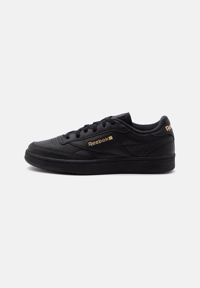 Μαύρο sneaker Reebok χαμηλού τύπου με χρυσό λογότυπο στο πλάι και στη φτέρνα, σχεδιασμό με κορδόνια και υφασμένο πέλμα σε λευκό φόντο.