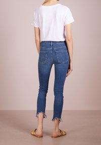 Camiseta blanca de manga corta combinada con jeans de mezclilla de un azul medio, elásticos y con el dobladillo deshilachado, llevados con sandalias amarillas de tipo slide.