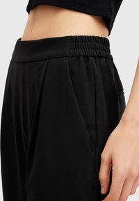 Pantaloni neri con una ampia vita elastica, davanti plissettato e tasche laterali, realizzati in un tessuto liscio e leggero.