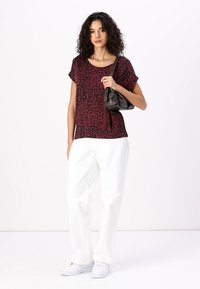 T-shirt léopard rouge et noir à manches courtes, associé à un pantalon blanc à jambes larges et des baskets blanches, portant un petit sac noir.