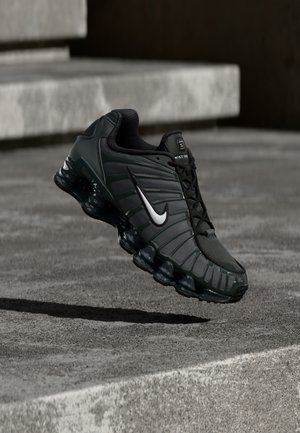 Pantofi sport Nike de culoare verde închis, cu un superior sintetic neted, textură din plasă, șireturi negre și o talpă lucioasă cu amortizare de aer.