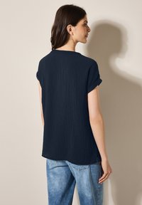 T-shirt blu navy a costine con maniche corte arrotolate, scollatura rotonda e vestibilità rilassata, abbinato a jeans blu chiaro.