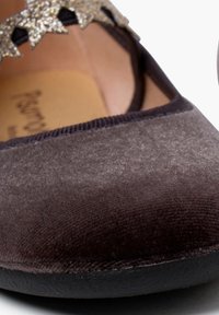 Ciemnobrązowe, aksamitne płaskie buty z zaokrąglonym noskiem, z czarną gumową podeszwą i błyszczącym, złotym akcentem w kształcie gwiazdki na podbiciu.