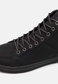 Baskets montantes noires en cuir texturé, œillets en métal et lacets gris. La semelle est lisse avec un léger motif de bande de roulement.