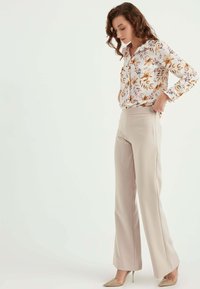 Bloemige blouse met een witte achtergrond en herfstkleuren, gecombineerd met beige wijde pijpen broek en beige puntige hakken.