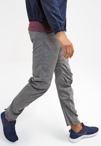 Šedé kalhoty slim fit, s hladkou texturou a bočními kapsami. Nosené s námořnickou bundou a tmavými sportovními botami.