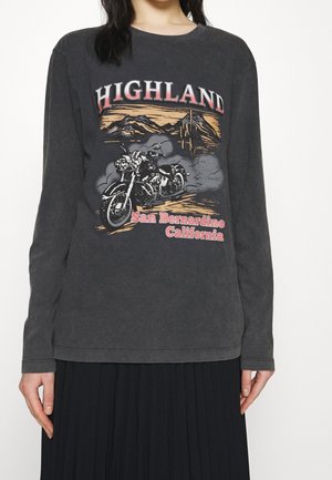 Camiseta de manga larga gris oscuro con un gráfico de motocicleta, montañas y texto "HIGHLAND San Bernardino California" usada por una persona.