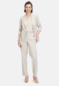 Licht beige op maat gemaakte blazer en broeken set, met een geweven structuur, gecombineerd met een doorschijnende crèmekleurige blouse en gouden hoge hakken.