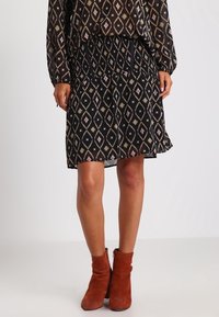 Jupe noire avec une taille élastique, présentant un motif en losanges géométriques rose et doré, associée à des bottines rouges à la cheville.