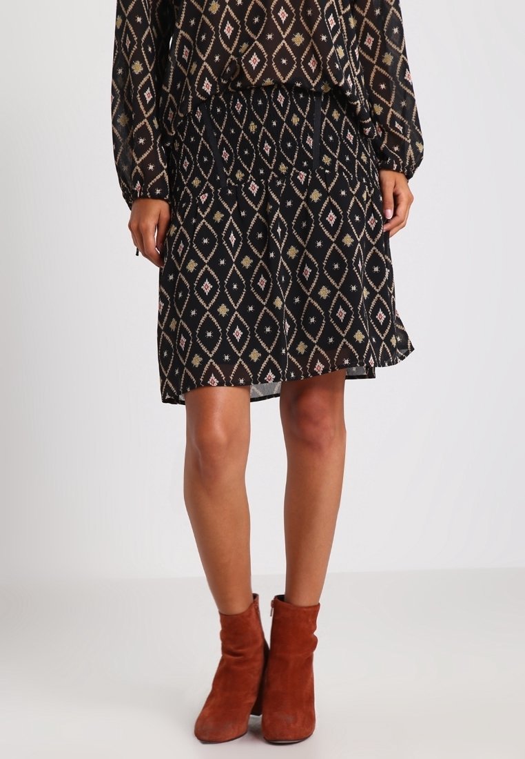 Jupe noire avec une taille élastique, présentant un motif en losanges géométriques rose et doré, associée à des bottines rouges à la cheville.