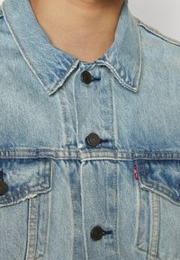 Ljusblå denimjacka med krage, framknappningar, två bröstfickor och röd Levi's-märklapp på vänster ficka.