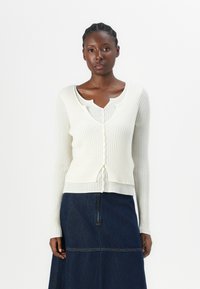 Hvit ribbet cardigan med lange ermer, med v-hals og knappelukking. B�æres over en grå topp og kombinert med et denimskjørt.