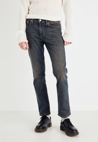 Mørkeblå denimjeans med rett snitt og svak fading, brukt sammen med en kremfarget teksturert genser og svarte snørebåndssko.