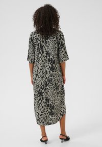 Robe à imprimé léopard, longueur genou en tissu gris clair avec une texture douce. Présente des manches amples et une coupe décontractée.