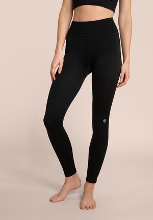 Leggings neri con una vita a costine e una texture liscia. Presentano un piccolo logo vicino alla caviglia. Design aderente, che arriva fino alle caviglie.