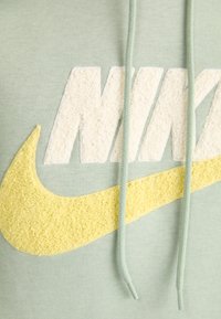Grön hoodie med en texturerad gul och crème Nike-logotyp, med snören och ett mjukt, bekvämt tyg.