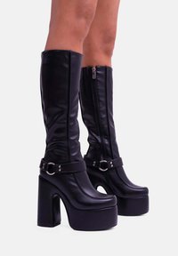 Stivali alti fino al ginocchio neri in finta pelle liscia, dotati di zip laterale, cinturino con fibbia e tacco spesso.