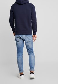 Felpa blu navy con orlo e maniche a coste, abbinata a jeans in denim azzurro. I jeans sono arrotolati ai polsini e presentano tasche posteriori.