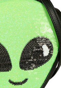 Volto di alieno verde con paillettes, grandi occhi neri e bianchi e una piccola bocca sorridente, bordato da un profilo in pelle nera.