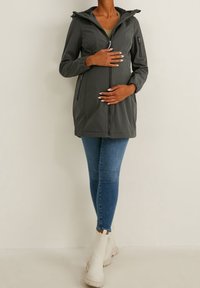 Grijze lange mouwen jas met een ritssluiting aan de voorkant, capuchon en zijzakken, gecombineerd met blauwe skinny jeans en witte enkellaarsjes. Glad, lichtgewicht stof.