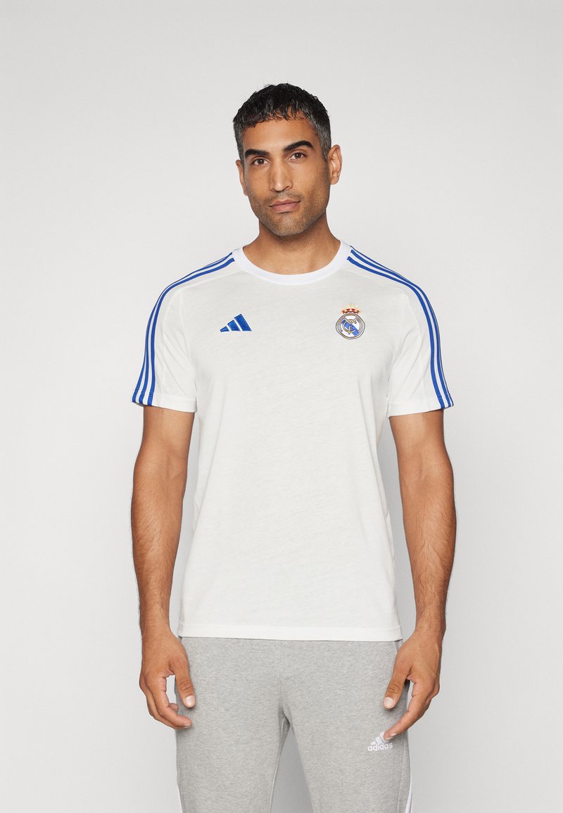 Bijela atletska majica s plavim prugama, s logotipom Real Madrida na prsima i Adidas oznakom na rukavu. Jednostavan dizajn.