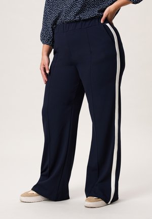 Marineblauwe wijde broek met een zachte textuur, voorzien van een witte zijstreep. Elastische tailleband voor comfort. Gedragen met casual sneakers.