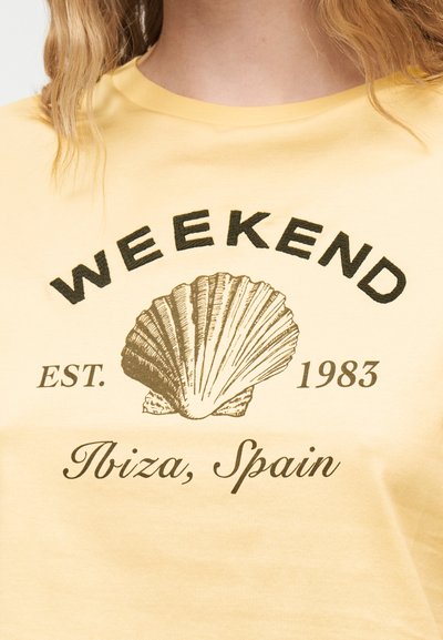 T-shirt jaune avec le texte "WEEK-END", un motif de coquillage, "EST. 1983" et "Ibiza, Espagne" imprimés sur le devant.
