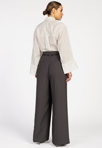Wit gestreept overhemd met lange mouwen en een hoge kraag, gecombineerd met donkergrijze wijde broek met een ceintuur in de taille en achterzakken.