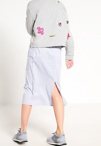 Sweatshirt gris avec des patchs, jupe midi rayée bleu et blanc avec une fente sur le côté, et baskets grises. Vue arrière de la tenue.