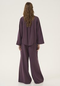 Purple, loose-fitting two-piece outfit with a long-sleeve top and wide-leg pants. Smooth texture, minimal detailing, and a relaxed silhouette.