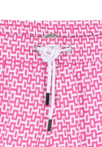 Costumi da bagno con un motivo geometrico rosa e bianco, cintura elastica con lacci bianchi e aghetti metallici.