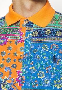 Färgglad polo skjorta med en blandning av blå och orange blommönster, med klassisk krage och knäppning. Bomullstyg.