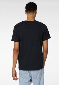 Svart bomull t-skjorte med korte ermer og rund hals. Glatt tekstur, avslappet passform, kombinert med lyseblå denimjeans.