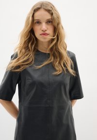 Abito in pelle nera con maniche corte, scollo rotondo e cuciture minime. Tessuto liscio con scollatura aderente e silhouette ampia.