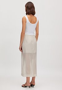 Lang, doorschijnende beige rok met een vloeiende design en een rechte snit, gecombineerd met een aansluitend wit tanktop en zwarte sandalen.