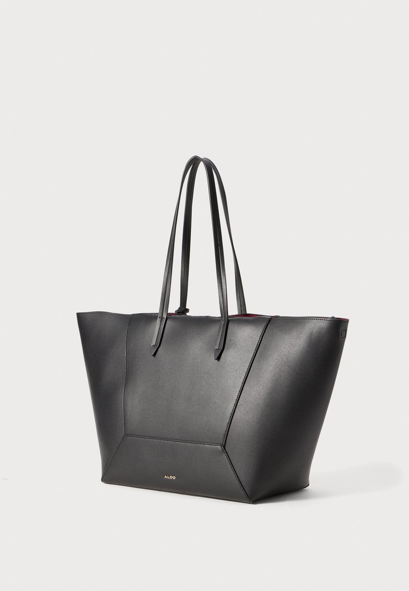Black leather tote bag with two flat handles, angular design, smooth texture, and a contrasting red interior. Features gold logo accent.
