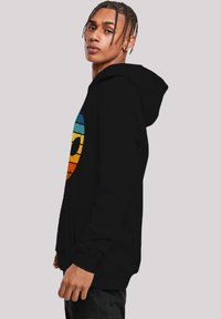 Schwarzer Hoodie mit einem großen Grafikdesign in Blau, Orange und Gelb, das einem Smiley ähnlich sieht. Verfügt über eine Fronttasche und gerippte Bündchen.