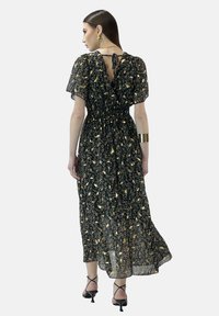 Robe maxi noire à motifs floraux, avec des manches courtes bouffantes, un col avec lien au dos, et une taille élastiquée, fabriquée dans un tissu léger et fluide.