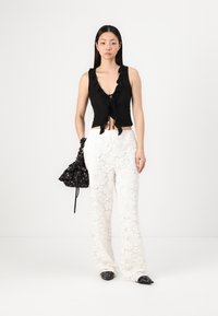 Top negru mulat cu margini volanate, decolteu în V, legat în față. Pantaloni albi din dantelă, cu croi larg, model floral. Geantă neagră cu flori, pantofi negri ascuțiți.