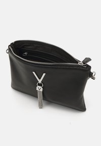 Černý kožený pouzdro se stříbrným zipem a dekorativním stříbrným přívěskem ve tvaru písmene V s visícími řetízky, zobrazené otevřené na bílém pozadí.