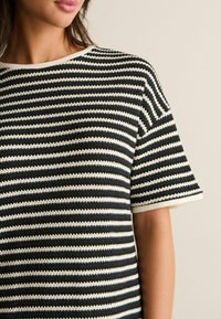 Prążkowany T-shirt z krótkim rękawem, z poziomymi czarnymi i kremowymi paskami, okrągłym dekoltem i teksturowanym materiałem.
